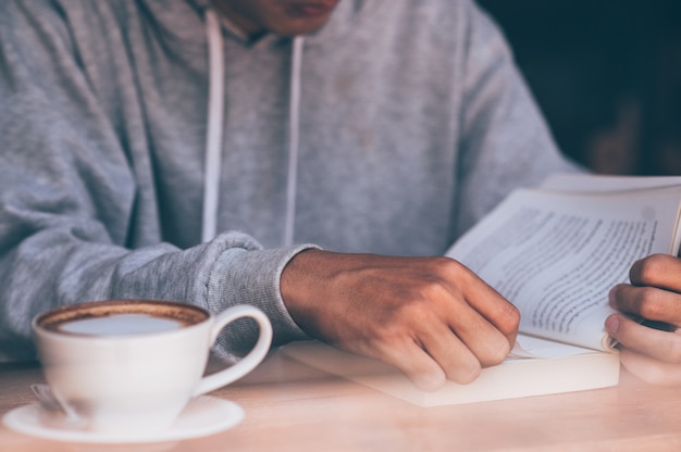 The young man sat on the couch and read a book while sipping a hot coffee.