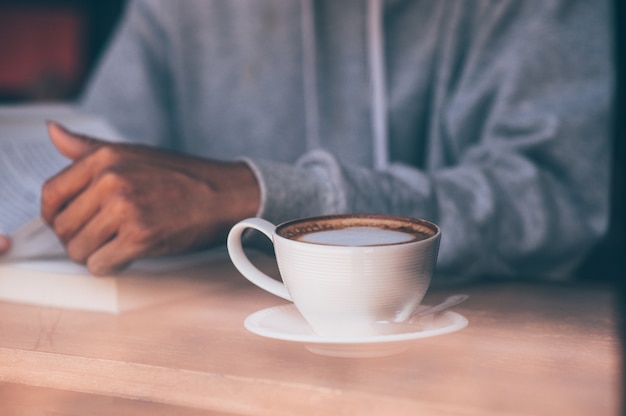 The young man sat on the couch and read a book while sipping a hot coffee. 