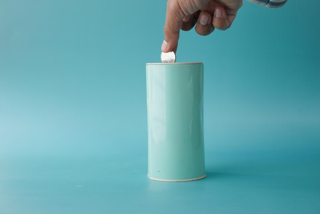 Young man saving coins in a jar on light green background