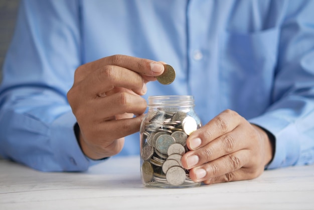 Young man saving coins in a jar white sited