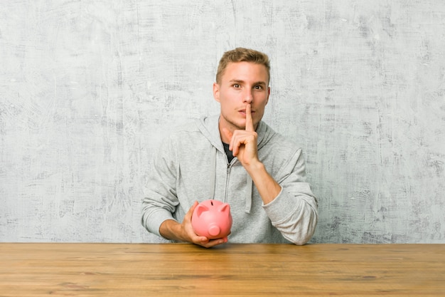 Young man saving money with a piggy bank keeping a secret or asking for silence.