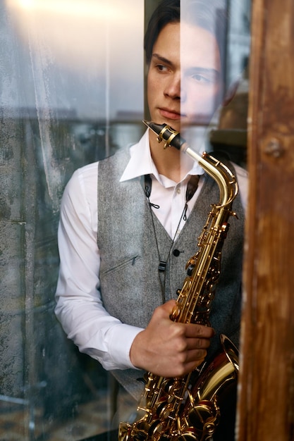 Young man saxophonist with instrument view from window