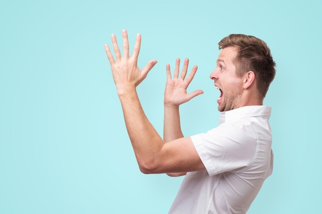 Young man screaming aside with hands gesture isolated on blue background