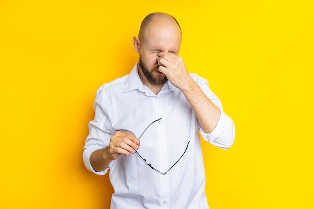 Young man screwing up his eyes and taking off his glasses on a yellow background