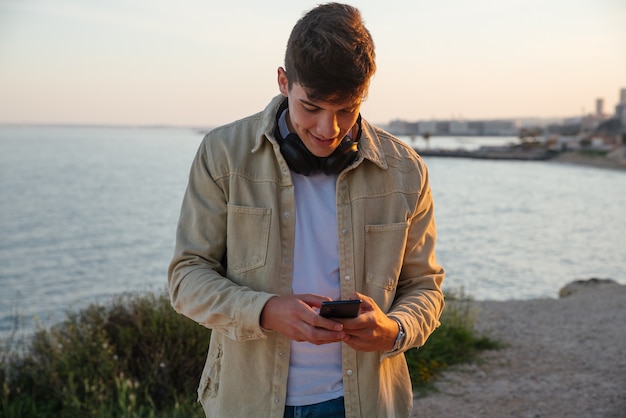 Young man searches music with his mobile phone and listens with headphones outdoors