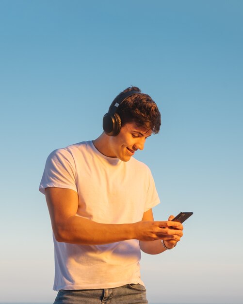 Young man searches music with his mobile phone and listens with headphones outdoors