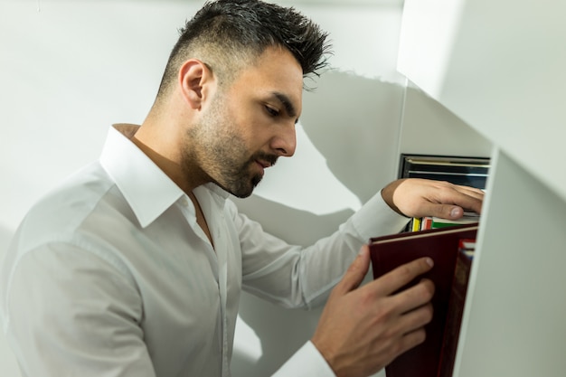 Young man searching for the right book at library shelf