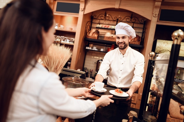 Giovane uomo che vende torte e tè alla donna in panetteria