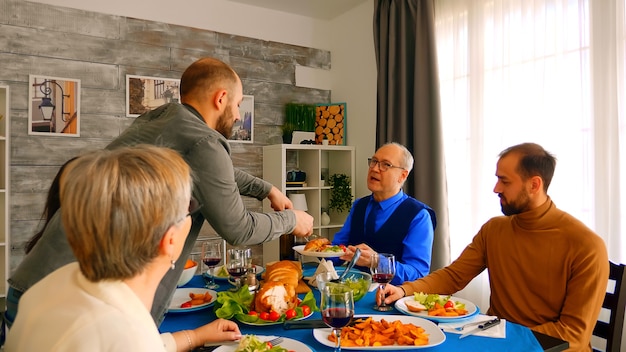 夕食時に鶏肉の大きなスライスで彼の父に仕える若い男。