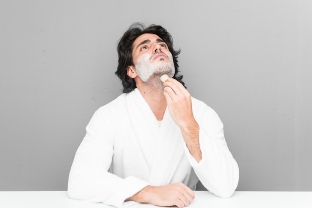 Young man shaving his beard on a grey