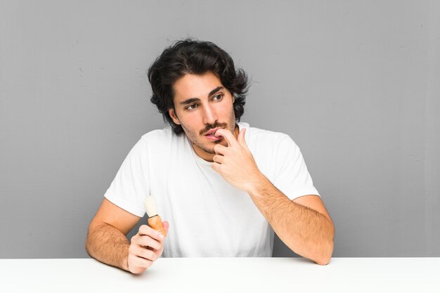 Young man shaving his beard relaxed thinking about something looking at a blank space.