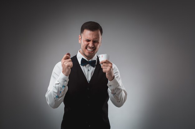 Young man in shirt and waistcoat shows his cards and holds poker chips in his hands, studio shot