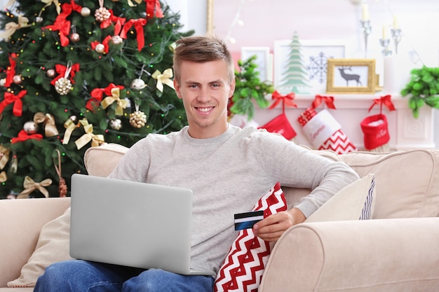 Молодой человек делает покупки в Интернете с помощью кредитной карты дома на Рождество