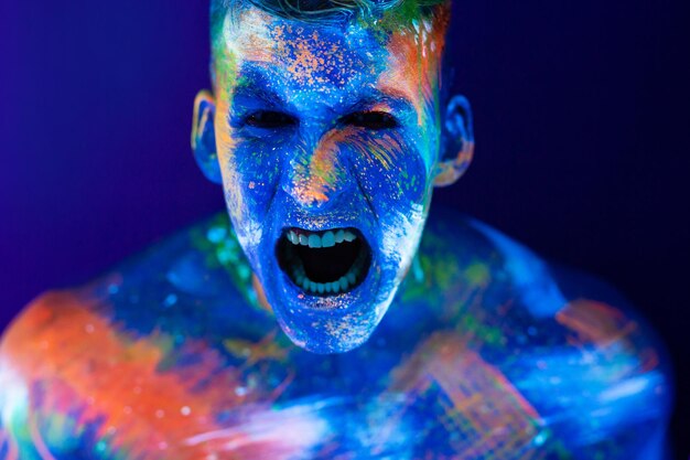 Young man shouts. Fluorescent paint on face and muscular torso, in studio shot with UV light