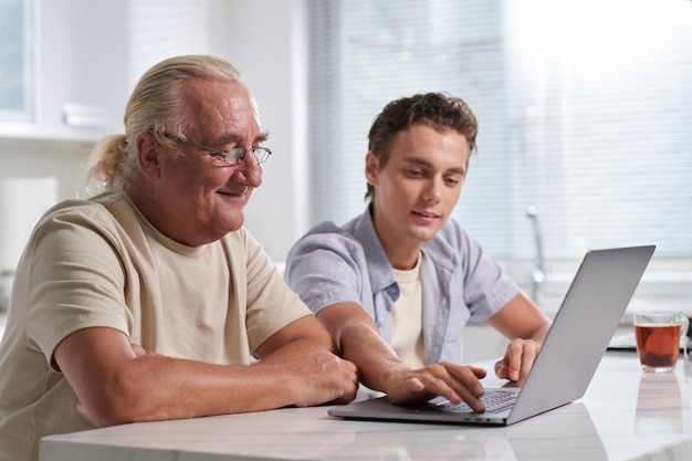 노인 할아버지 에게 노트북 에서 여러 가지 응용 프로그램 을 사용하는 방법 을 보여 주는 젊은 남자