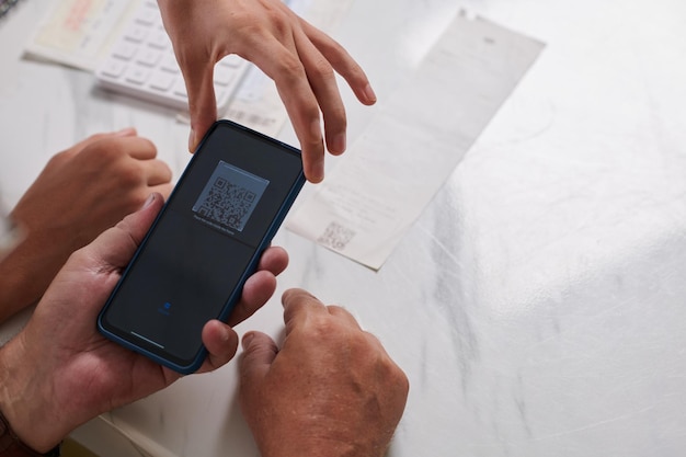 Молодой человек показывает дедушке, как сканировать QR-код на счете за коммунальные услуги для оплаты через мобильное приложение