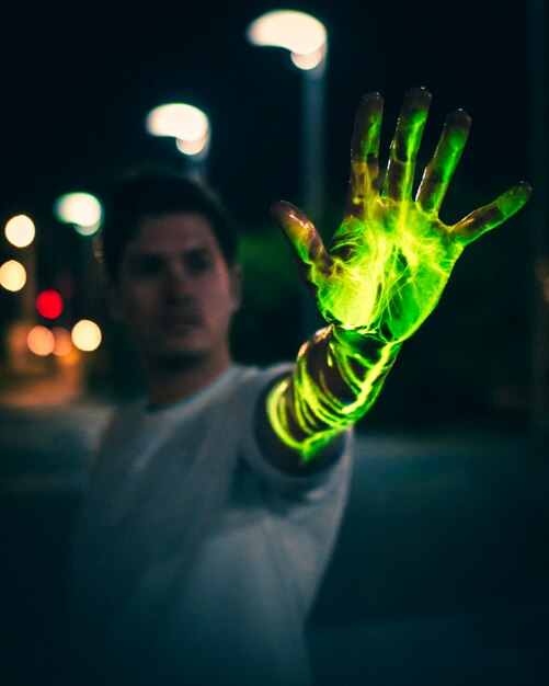 Foto giovane che mostra la mano verde luminosa di notte