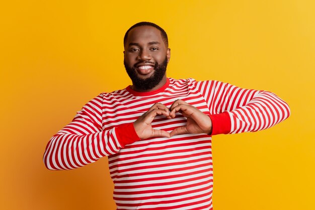 Young man showing heart gesture with hands beaming smiling on yellow wall