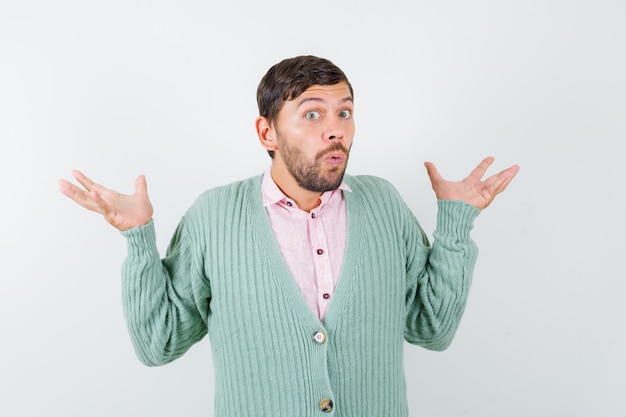 Young man showing helpless gesture in shirt, cardigan and looking bewildered , front view.