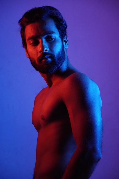 Young man showing his physic with headphone in neon light