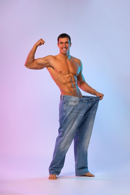 Молодой человек показывает, сколько веса он потерял с большими джинсами, толстыми, чтобы соответствовать концептуальному фитнес-постеру