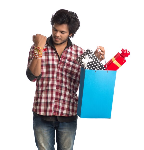 Young man showing rakhi on his hand with shopping bags and gift box on the occasion of Raksha Bandhan festival.