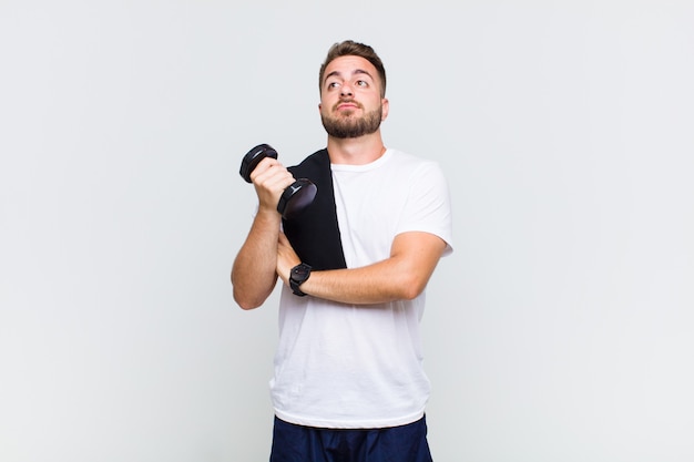 Young man shrugging, feeling confused and uncertain, doubting with arms crossed and puzzled look