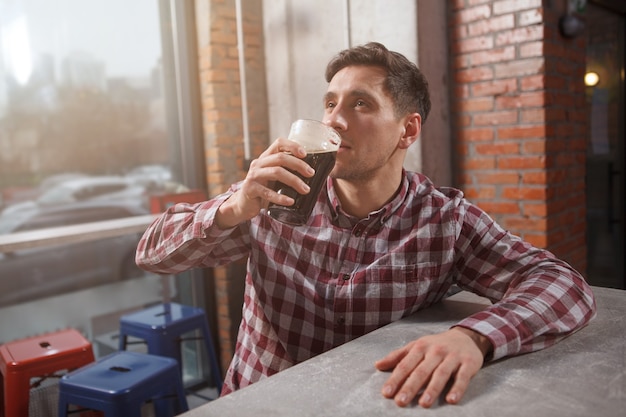 Giovane uomo sorseggiando una deliziosa birra artigianale, rilassante al pub birra, copia dello spazio