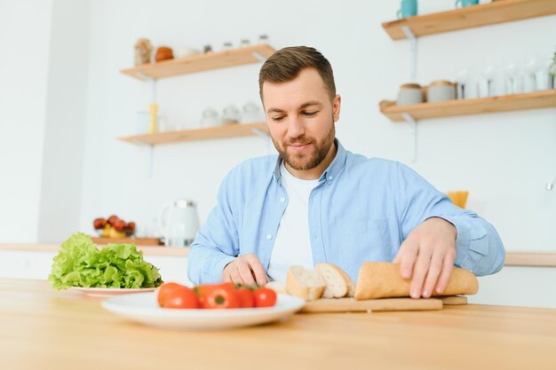 Young man sit at table and cut cucumber on salad