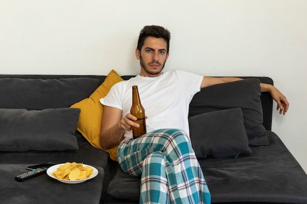A young man sits at home on the couch and watches TV.