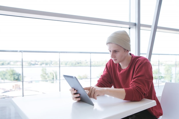 Young man sits in a light cafe with a tablet in his hands and makes a swipe on the screen