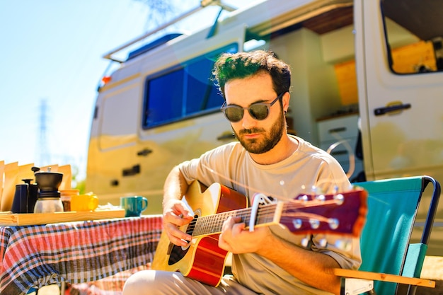 Young man sits near trailer truck and playing guitar