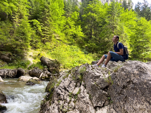 A young man sits on a rock by a mountain river