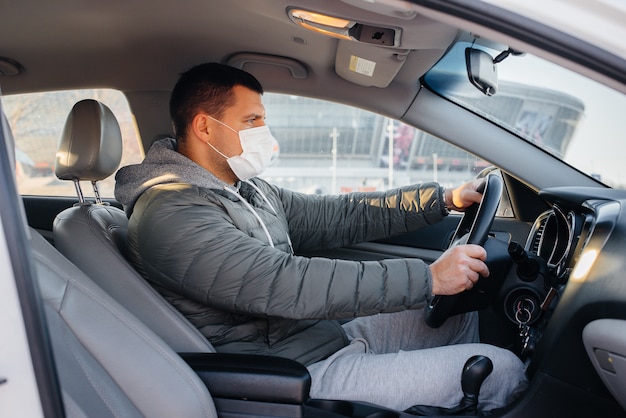 A young man sits behind the wheel wearing a mask for personal safety while driving during a pandemic and coronavirus. Epidemic.