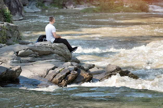 渦巻く川の土手に座っている若い男