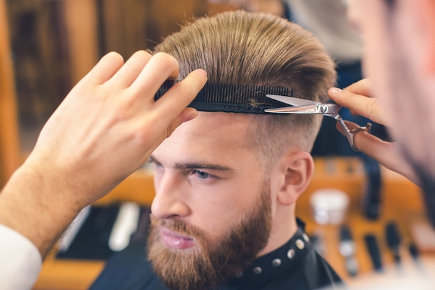 Young man sitting in a barbershop while barber cutting the hair