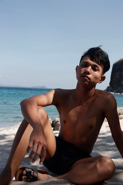 Photo young man sitting on beach against sky