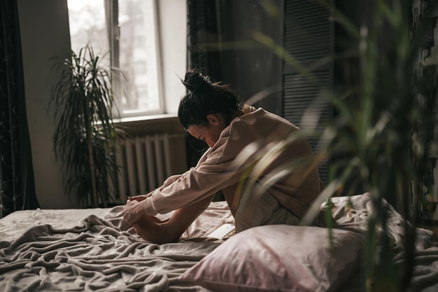 Young man sitting on bed against window