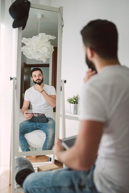 Photo young man sitting on the bed looking at himself in the mirror