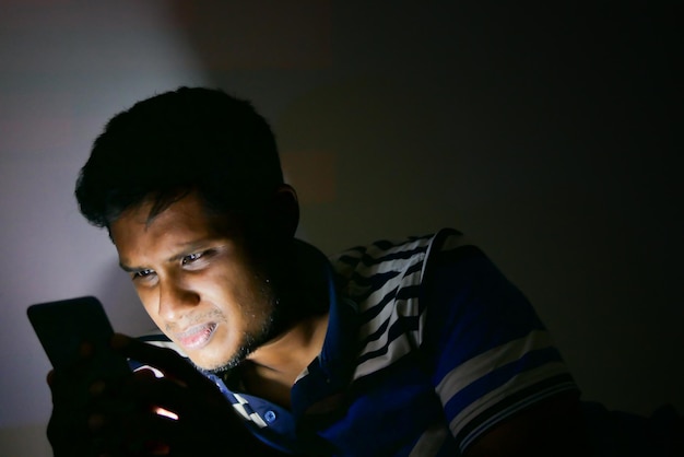 Young man sitting on bed using smart phone at night