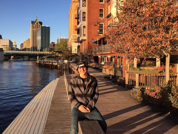 Photo young man sitting by lake on retaining wall in city