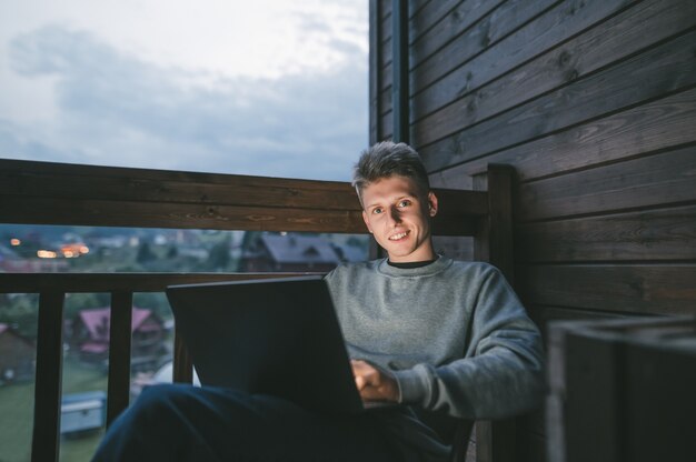 Young man sitting in a chair on a balcony using a laptop