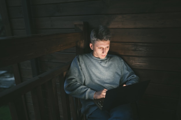 Young man sitting in a chair on a balcony using a laptop