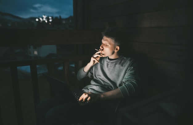 Young man sitting in a chair on a balcony using a laptop