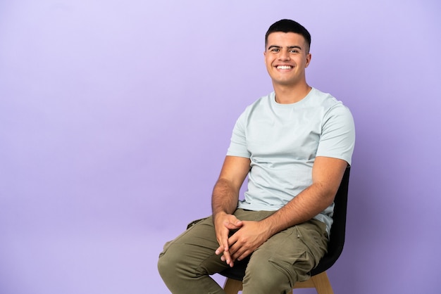 Young man sitting on a chair over isolated background laughing