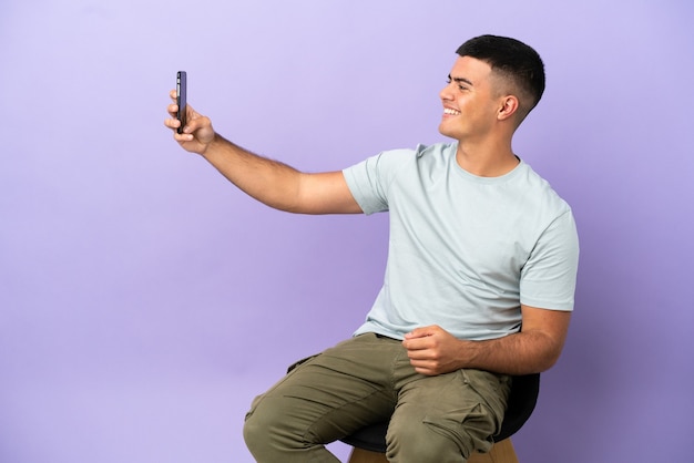 Young man sitting on a chair over isolated background making a selfie