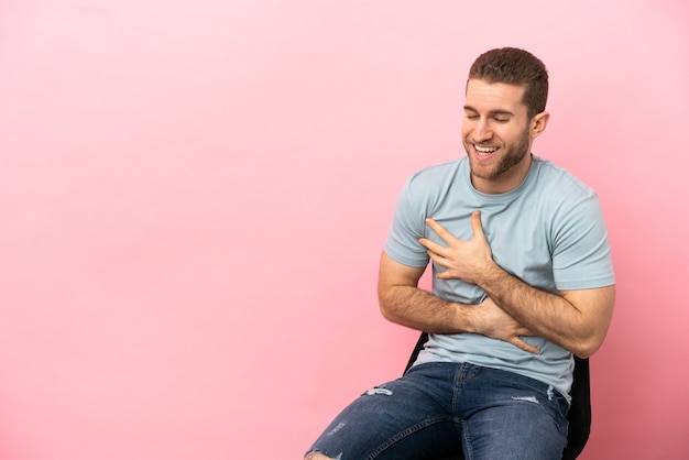 Young man sitting on a chair over isolated pink background smiling a lot