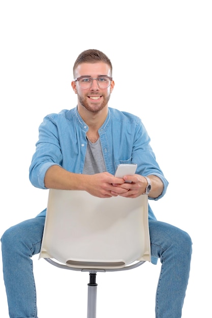 Молодой человек сидит на стуле и пользуется мобильным телефоном