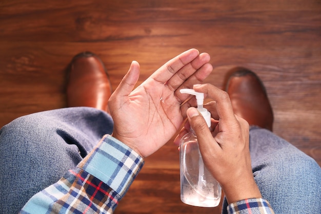 Giovane uomo seduto su una sedia utilizzando liquido disinfettante per prevenire il virus corona