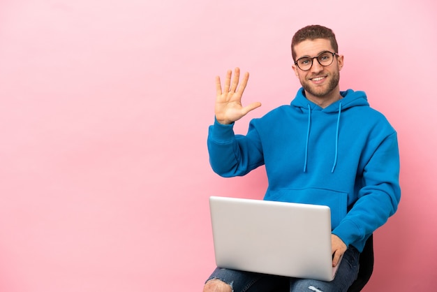 Giovane seduto su una sedia con un laptop che conta cinque con le dita